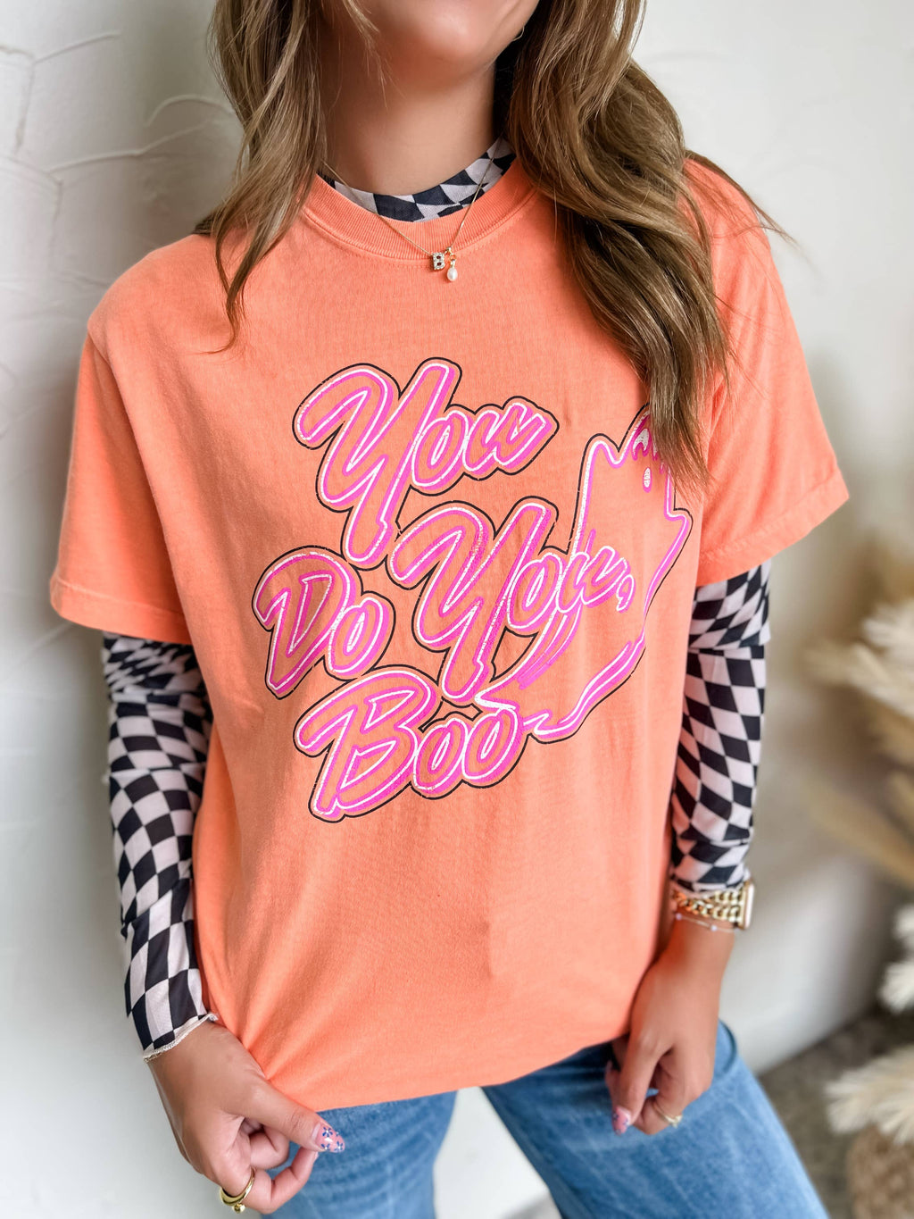 Person wearing an orange t-shirt with pink text, checkered sleeves, and blue jeans.